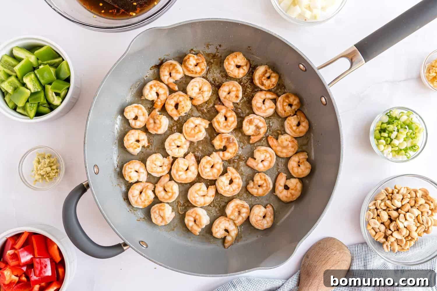 Fiery Peanut Shrimp Delight 8 Shrimp expertly cooking in a spacious frying pan, sizzling and turning pink, indicating they are almost ready.