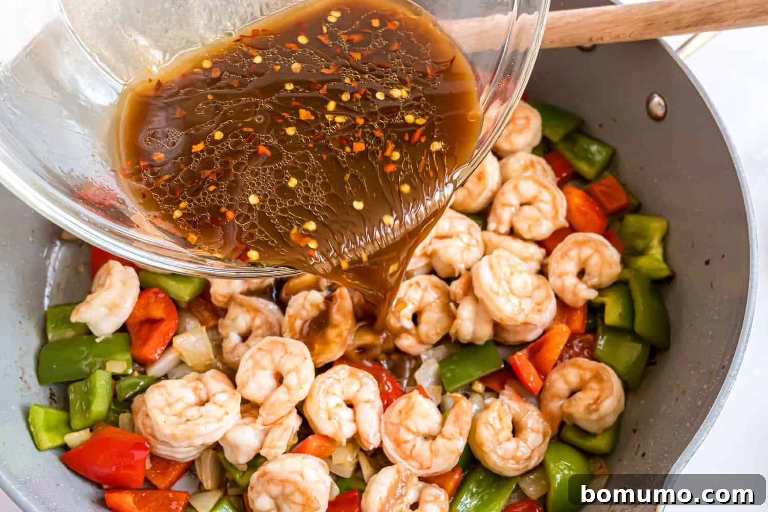 Fiery Peanut Shrimp Delight 10 The vibrant sauce being poured over the cooked shrimp and vegetables in the frying pan, about to be thickened.