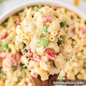 Chicken macaroni salad on a wooden spoon held over a large white bowl, garnished with fresh herbs.