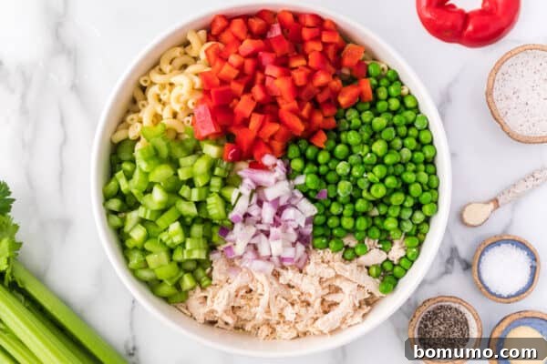 Chicken macaroni salad ingredients added to a large bowl with the dressing.