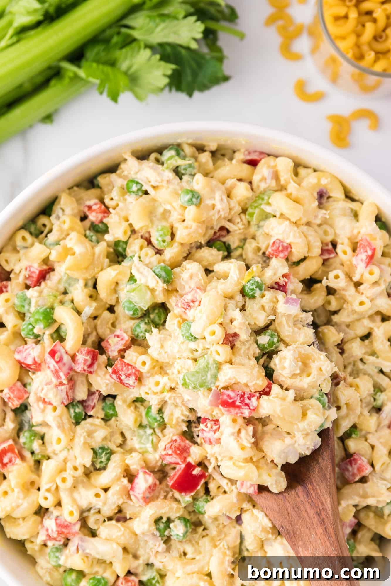 Overhead view of a spoonful of chicken macaroni salad resting in a large bowl, ready to be enjoyed.