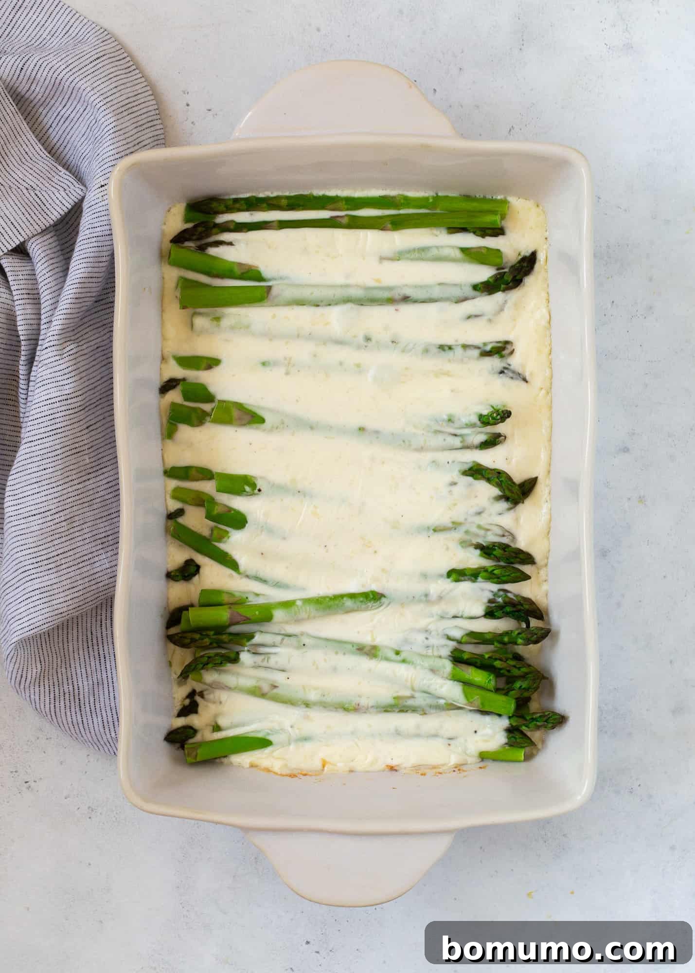 Creamy Asparagus Bake 12 Creamy cheese sauce poured over raw asparagus spears in a baking dish, before baking.