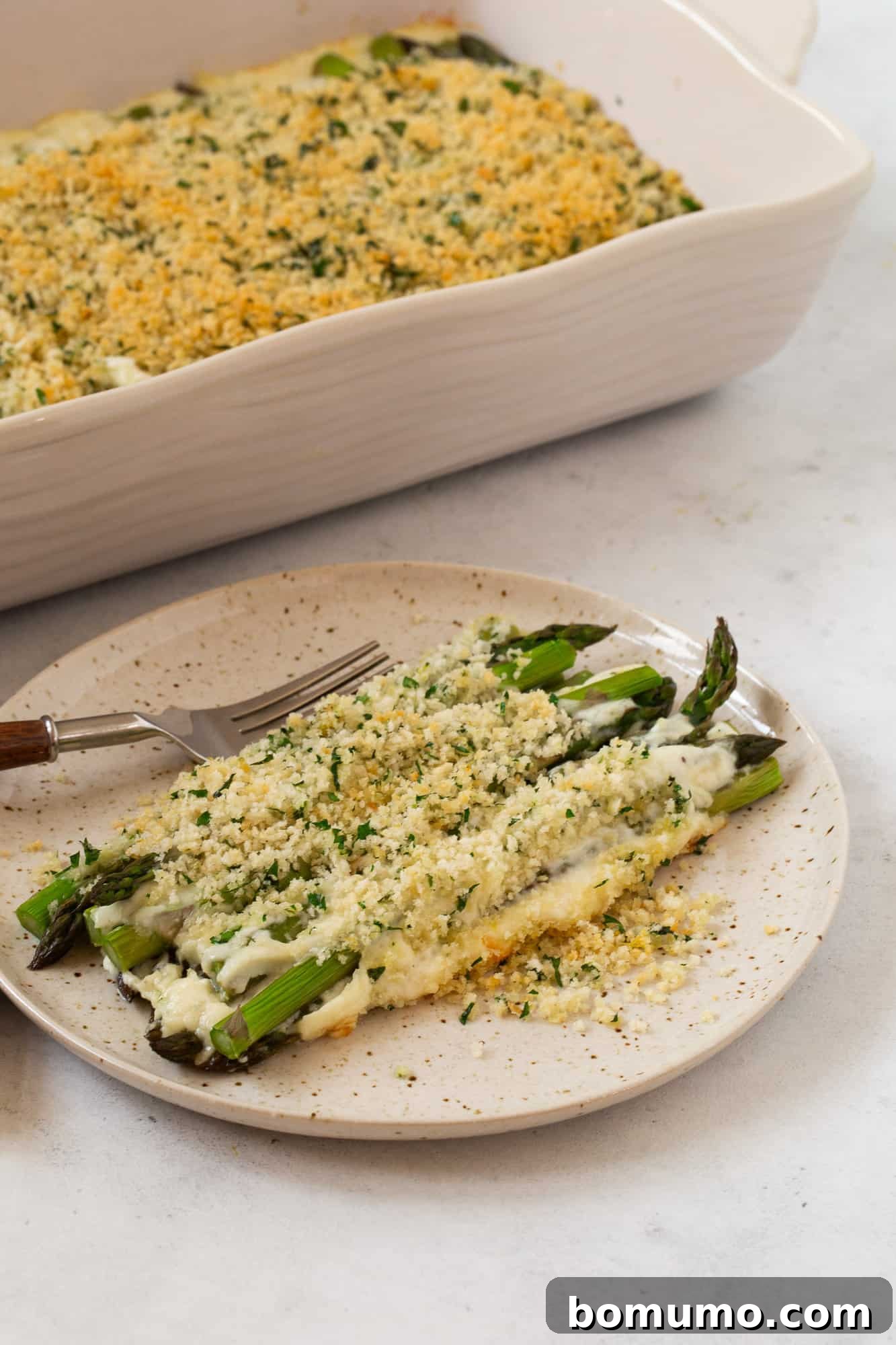 Creamy Asparagus Bake 18 Plated serving of asparagus casserole with more of the casserole in the background.
