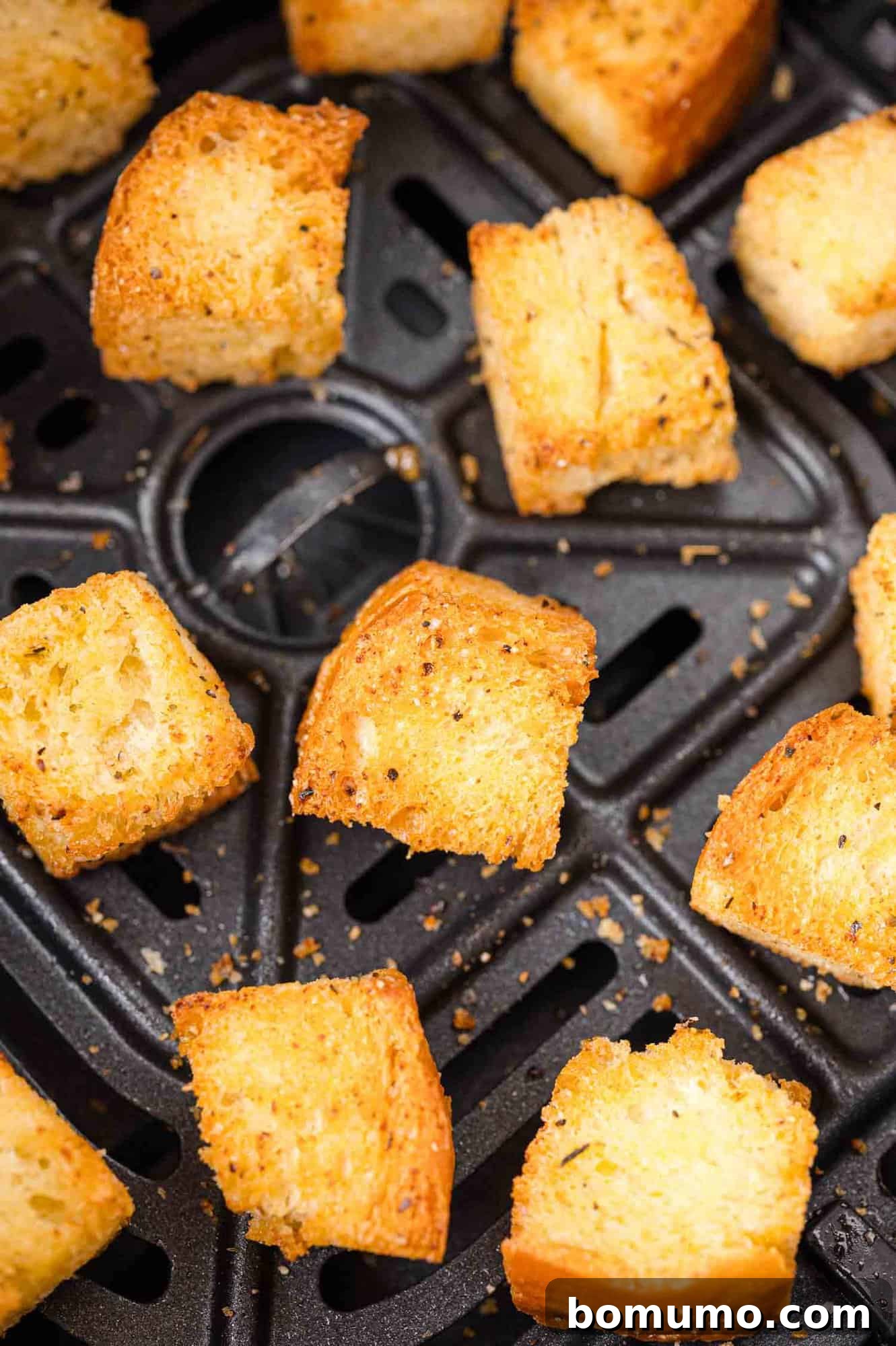 Golden-brown air fryer croutons evenly spread in a black air fryer basket.