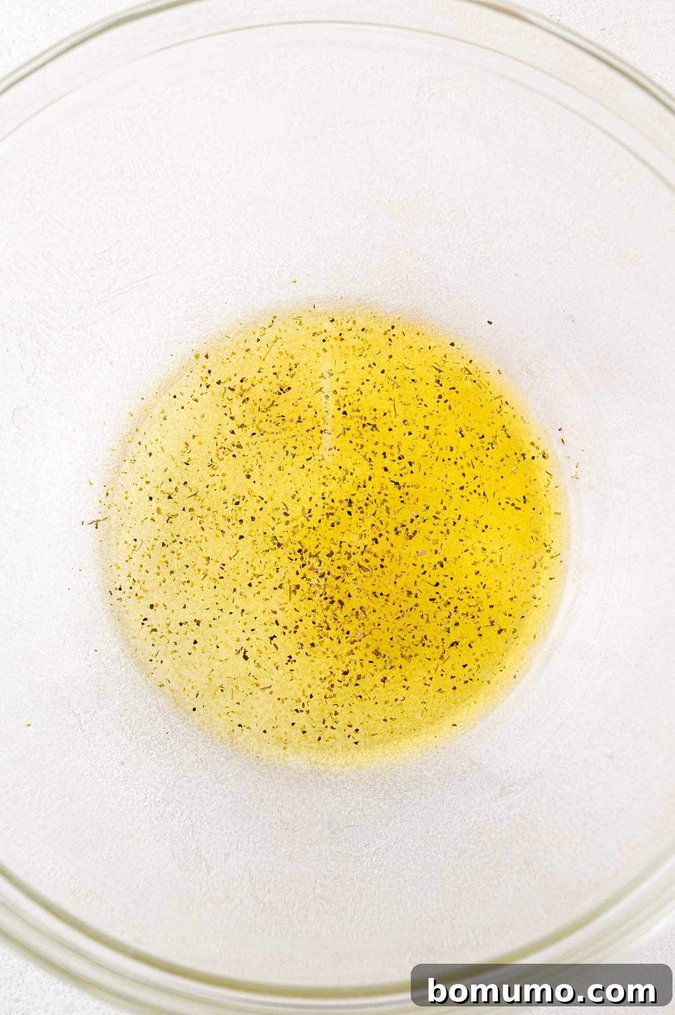 A bowl containing olive oil mixed with various seasonings, ready for bread.