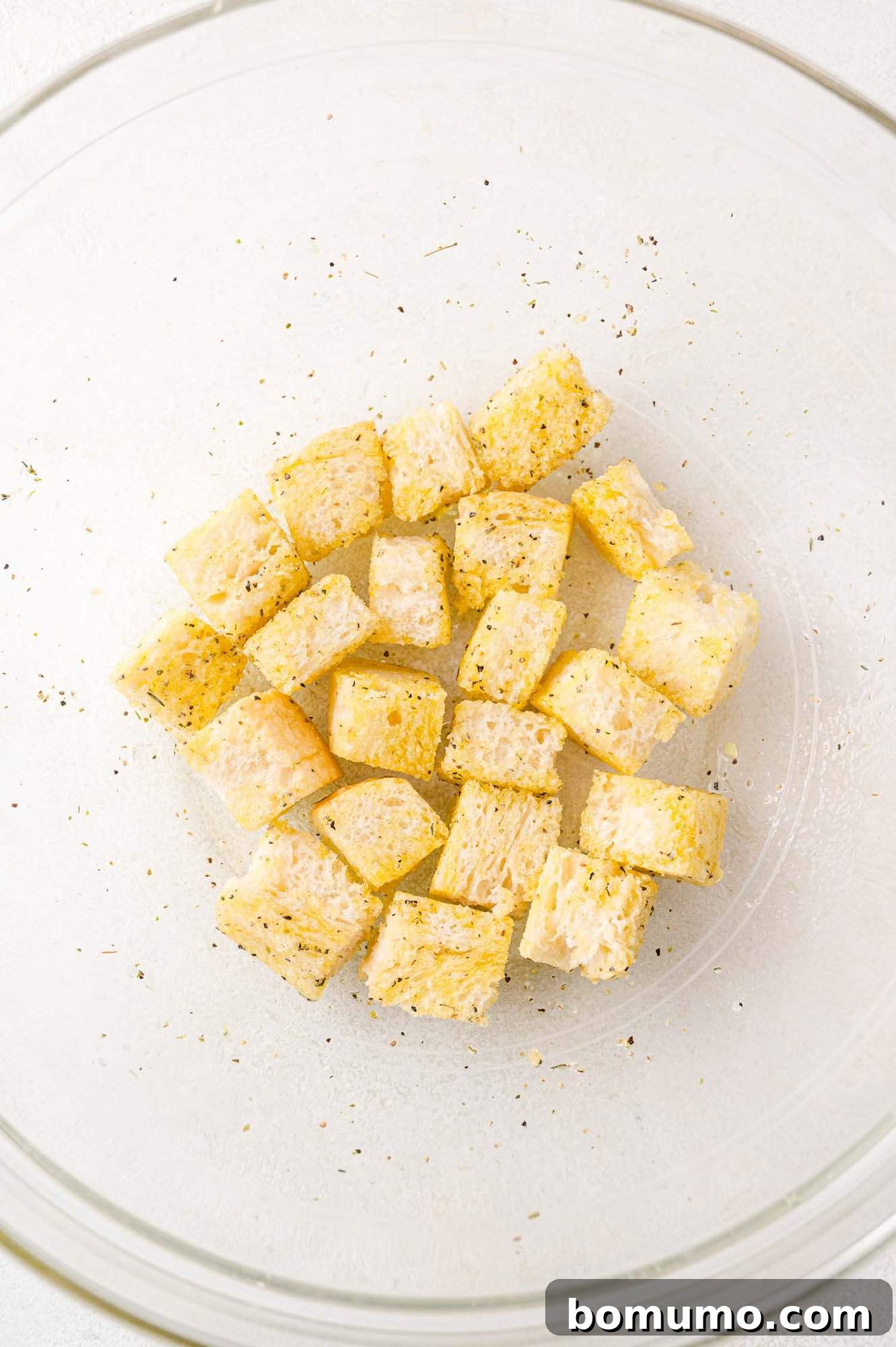 Bread cubes being tossed in a bowl with oil and seasonings, ensuring an even coating.