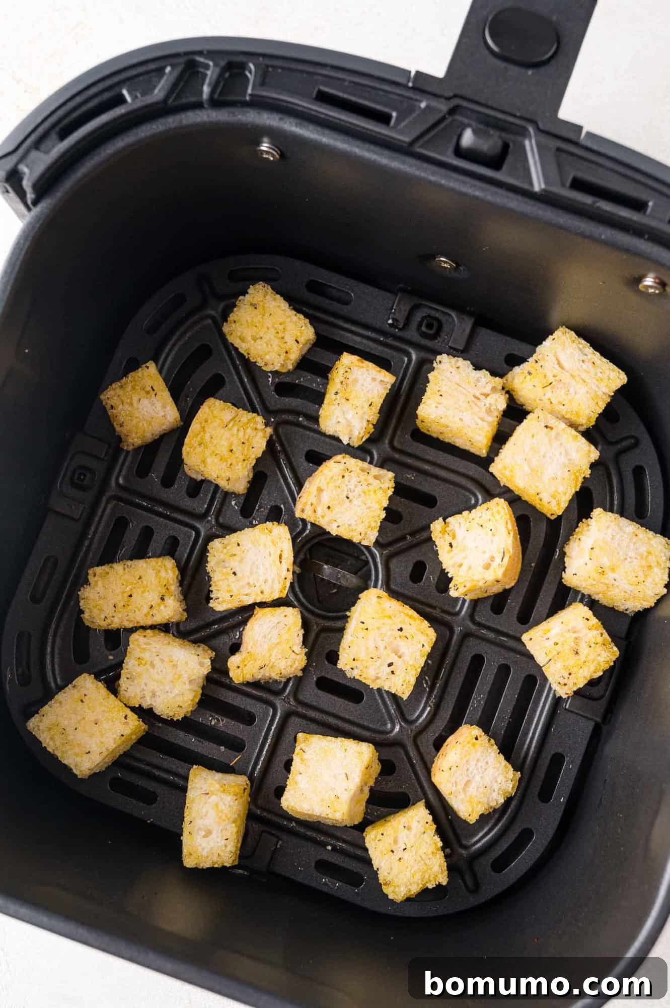 Uncooked seasoned bread cubes spread in a single layer in the air fryer basket.