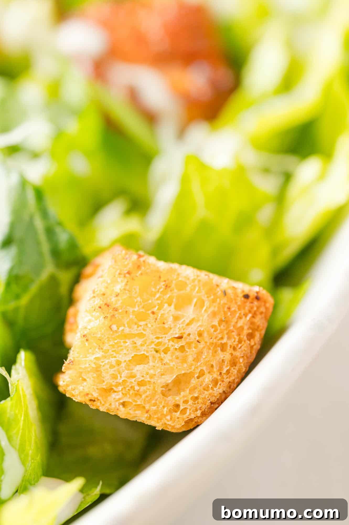 A close-up shot of a perfectly golden-brown air fryer crouton resting on a fresh green salad.