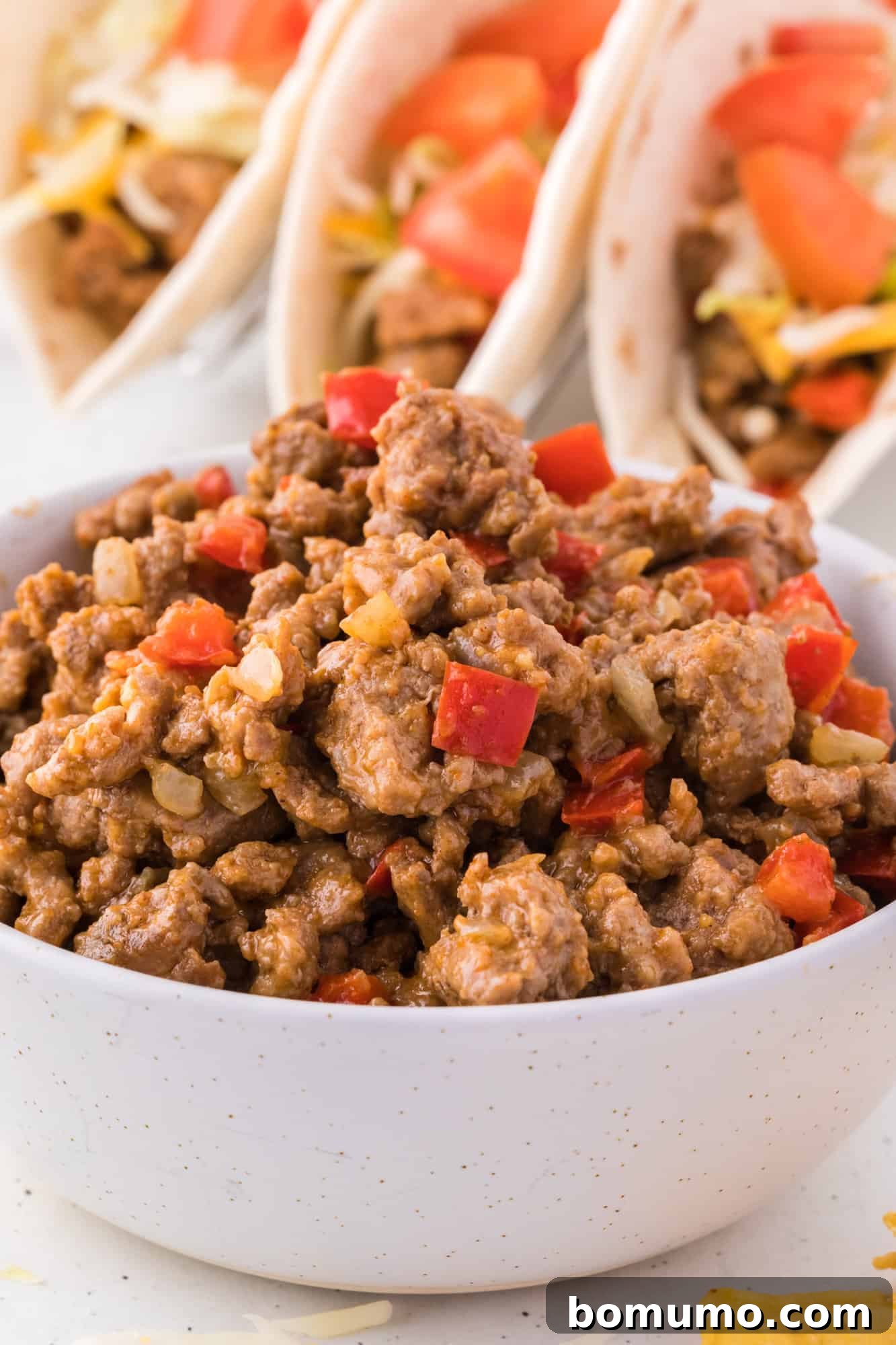 Ground turkey taco mean in a white bowl, with tacos in the background.