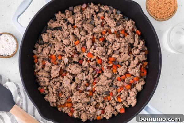 Ground turkey sauteing in a cast iron skillet with diced vegetables.
