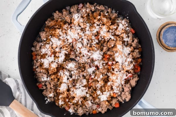 Flour sprinkled over sauteed ground turkey taco meat in a cast iron skillet.