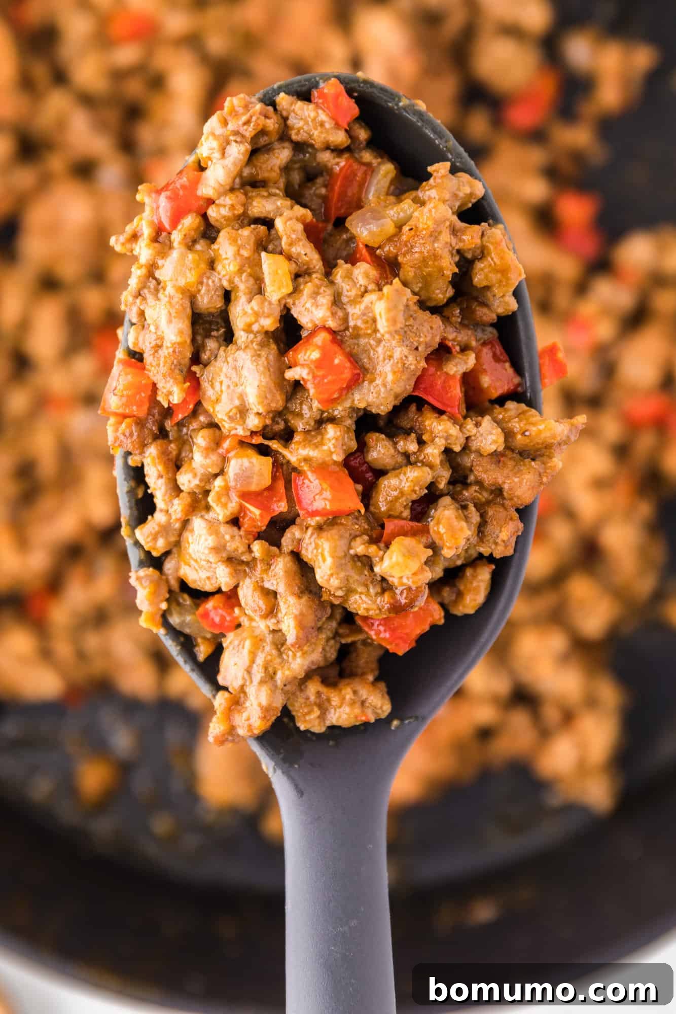 Close up of a spoonful of ground turkey taco meat held over more taco meat in a cast iron skillet.
