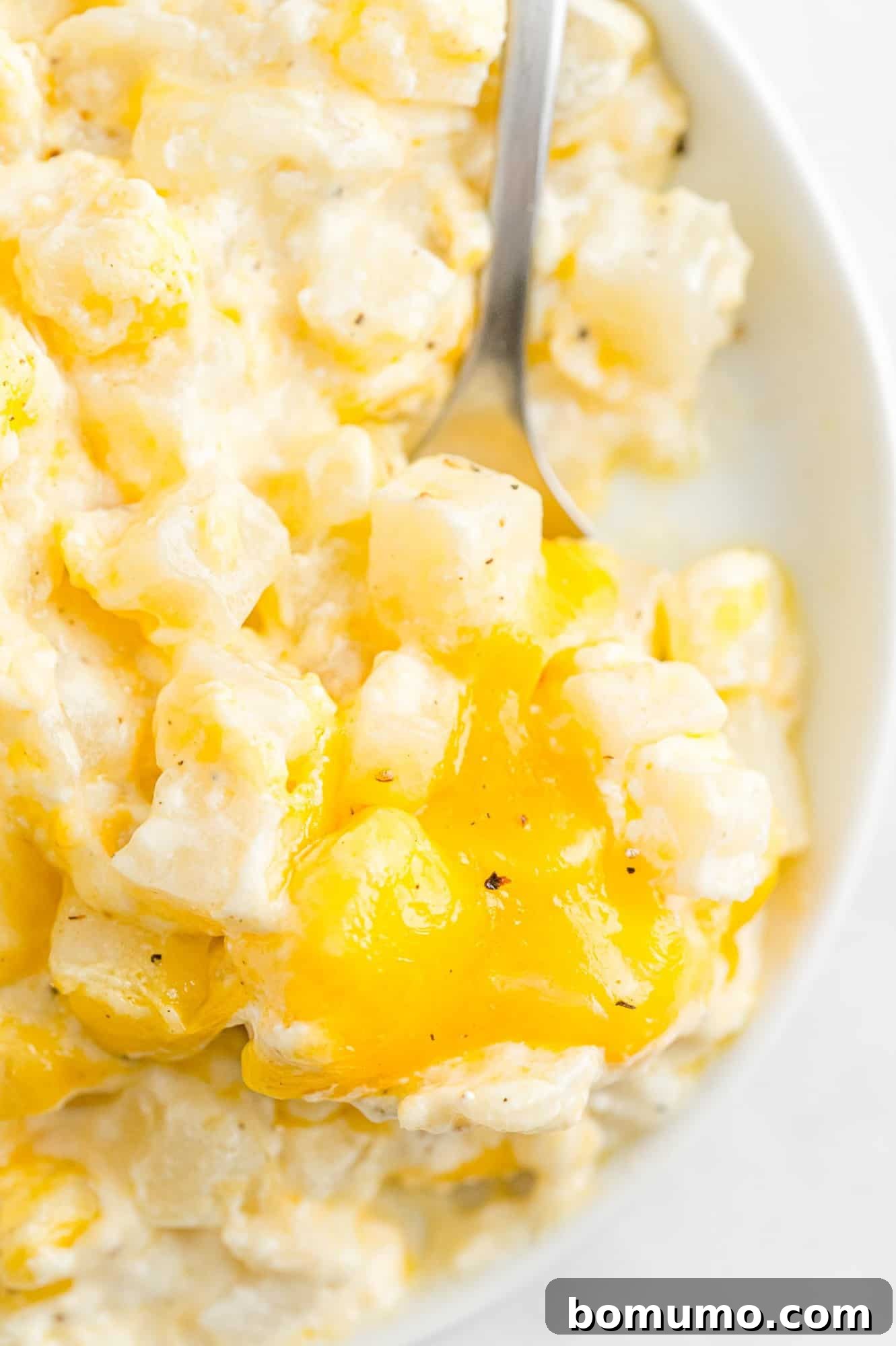 Slow cooker cheesy potatoes being scooped with a silver spoon.