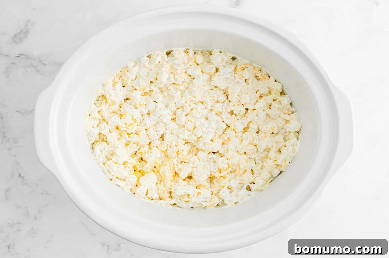 Uncooked crockpot cheesy potatoes in a white crockpot.