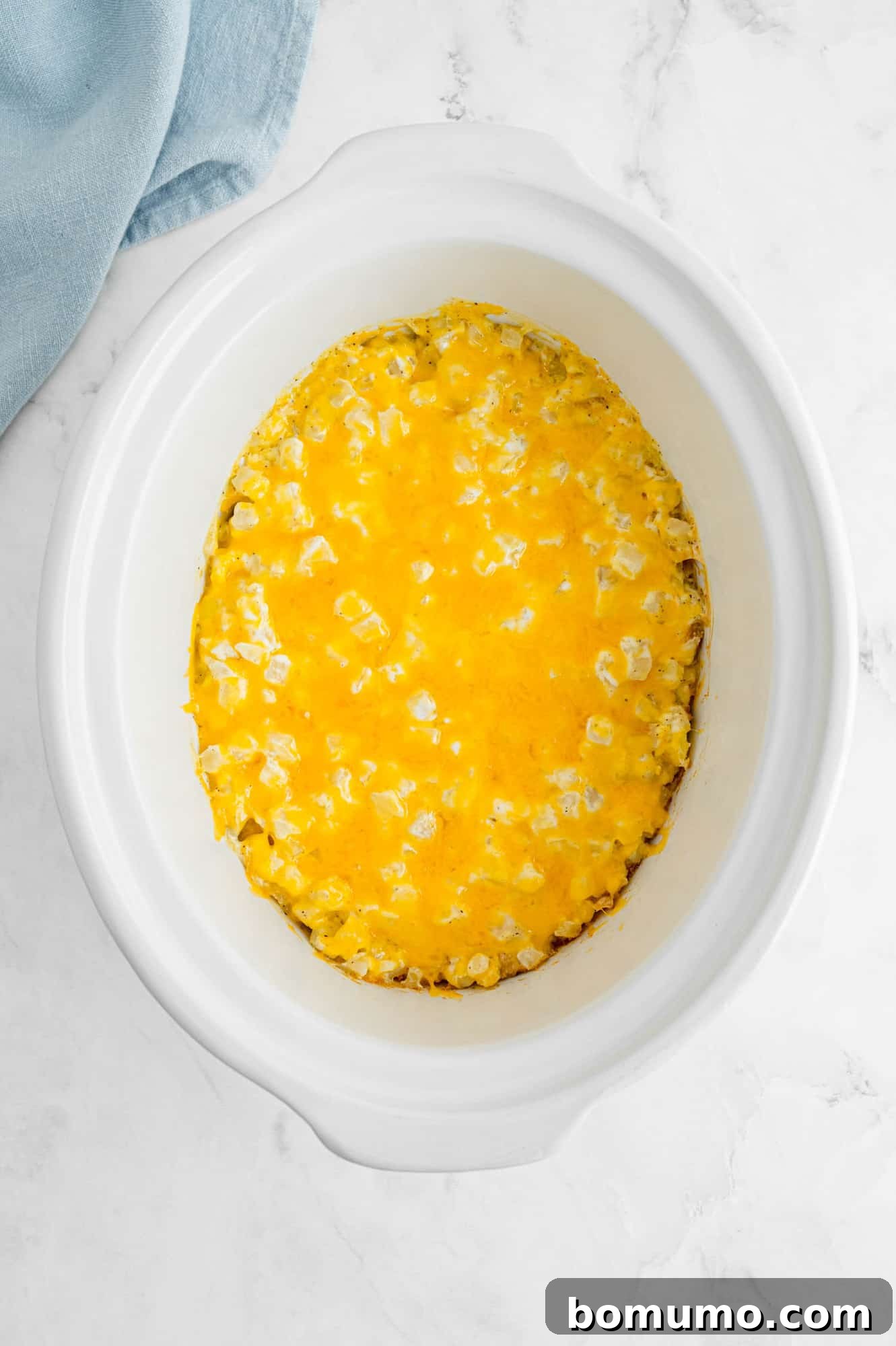 Crockpot cheesy potatoes with cheese melted on top, in a white slow cooker.