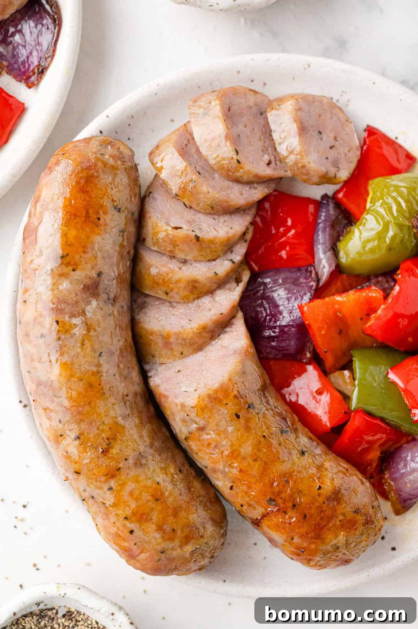 Delicious baked Italian sausage with tender peppers and onions, perfectly sliced and served on a plate, ready to enjoy as a quick and flavorful dinner.