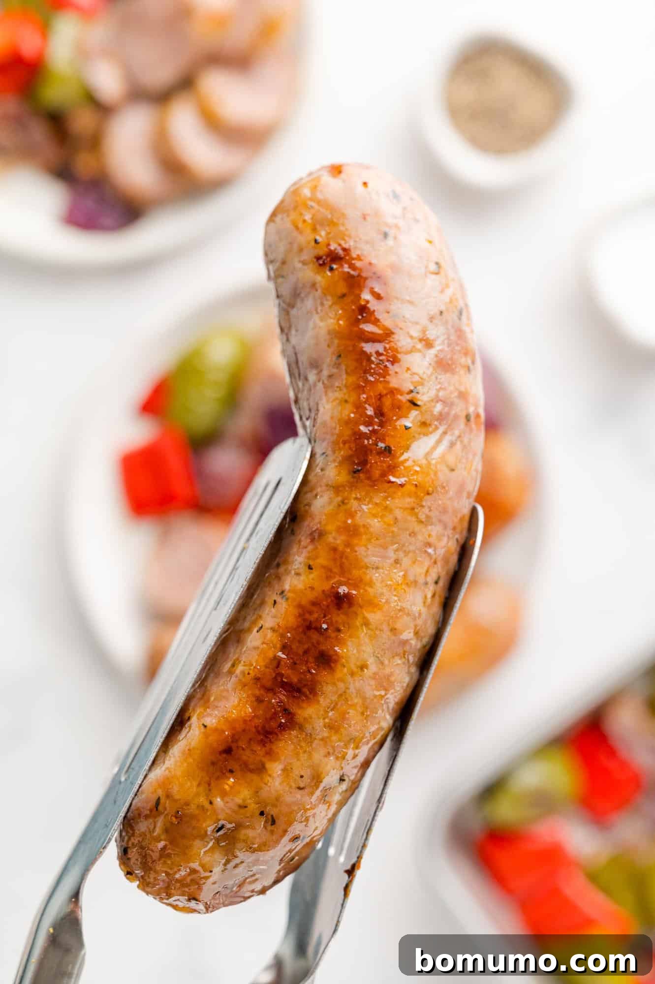 A perfectly cooked Italian sausage link held between tongs, showcasing its golden-brown exterior and readiness for serving.