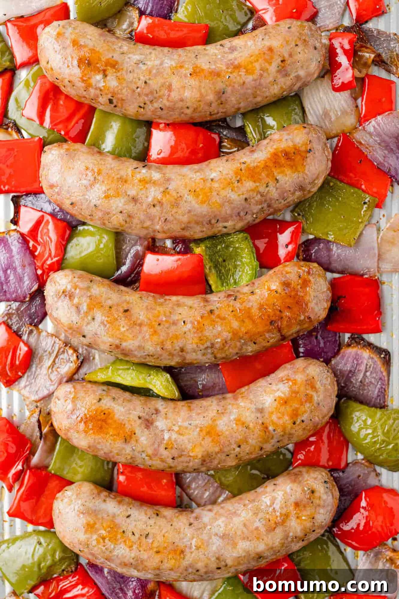 Perfectly cooked Italian sausage, vibrant bell peppers, and caramelized onions beautifully arranged on a sheet pan, fresh from the oven and ready to serve.