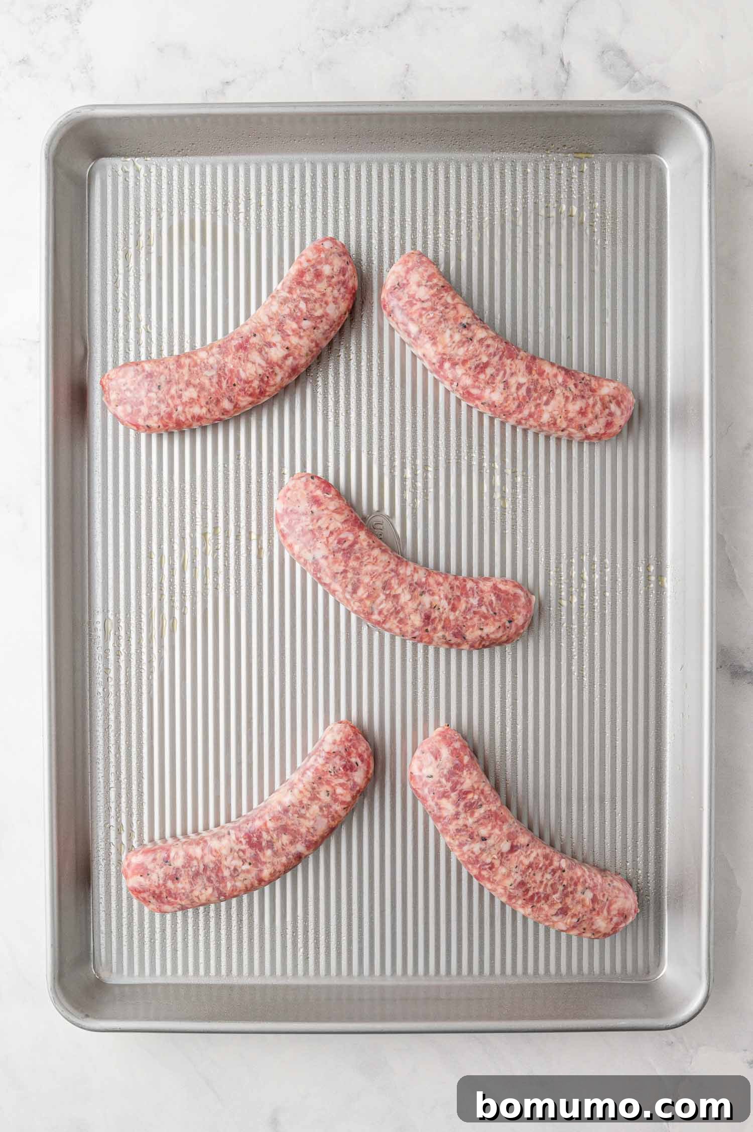 Raw Italian sausage links arranged on a prepared sheet pan, ready for baking.