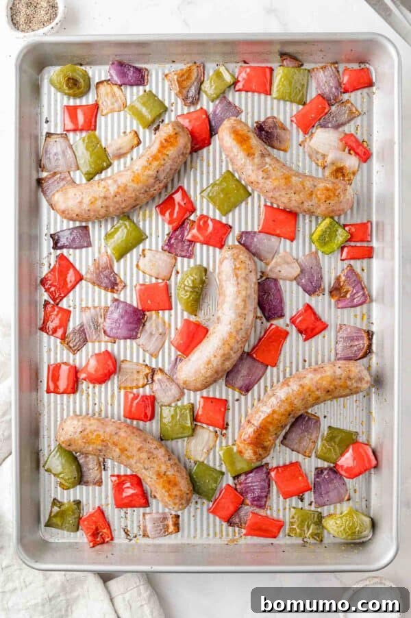 Fully cooked baked Italian sausage, bell peppers, and onions, caramelized and tender, still on the sheet pan after roasting, ready to be served.