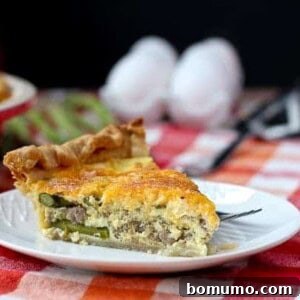 Slice of quiche on a round white plate. Eggs and fresh asparagus in the background.