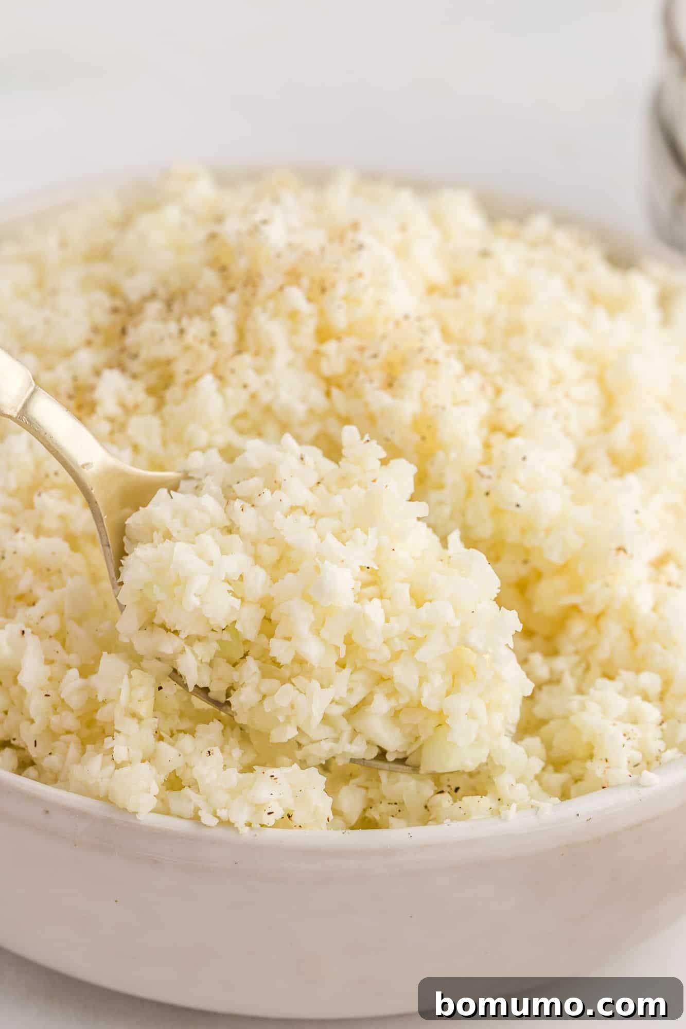 Close-up of riced cauliflower on a spoon, illustrating its perfect, fluffy texture, ready to be incorporated into various dishes.