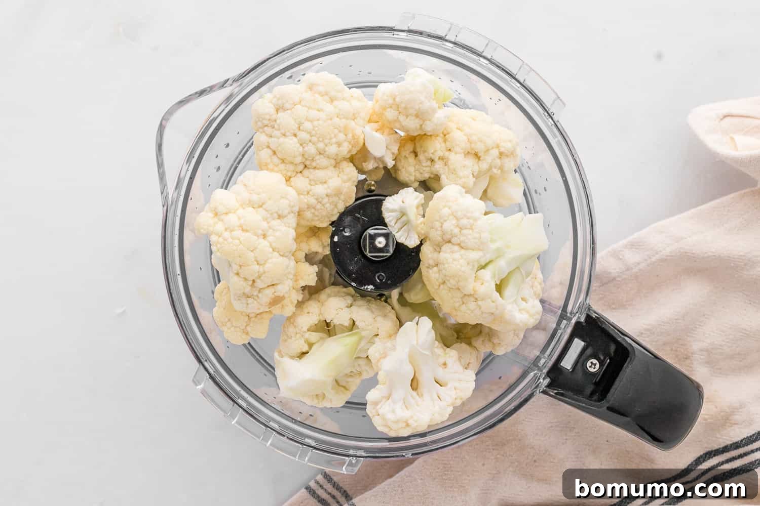 Cauliflower florets loaded into a food processor with the S-blade, prepared for processing into a rice-like consistency.