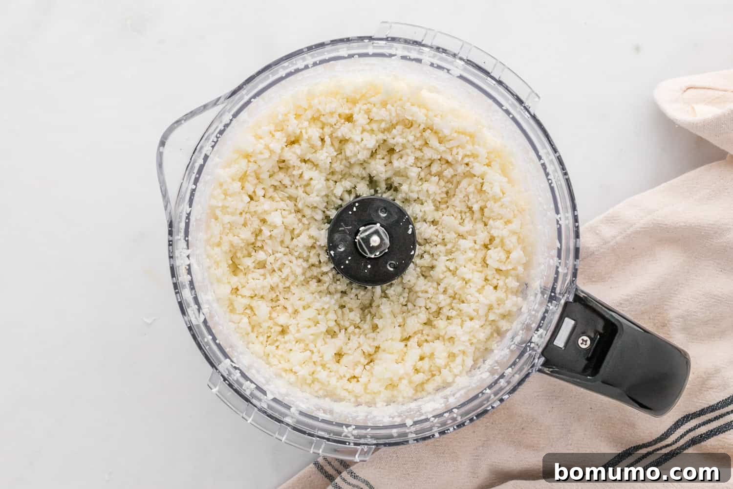 Finely riced cauliflower in a food processor, demonstrating the ideal texture achieved after pulsing, resembling grains of rice.