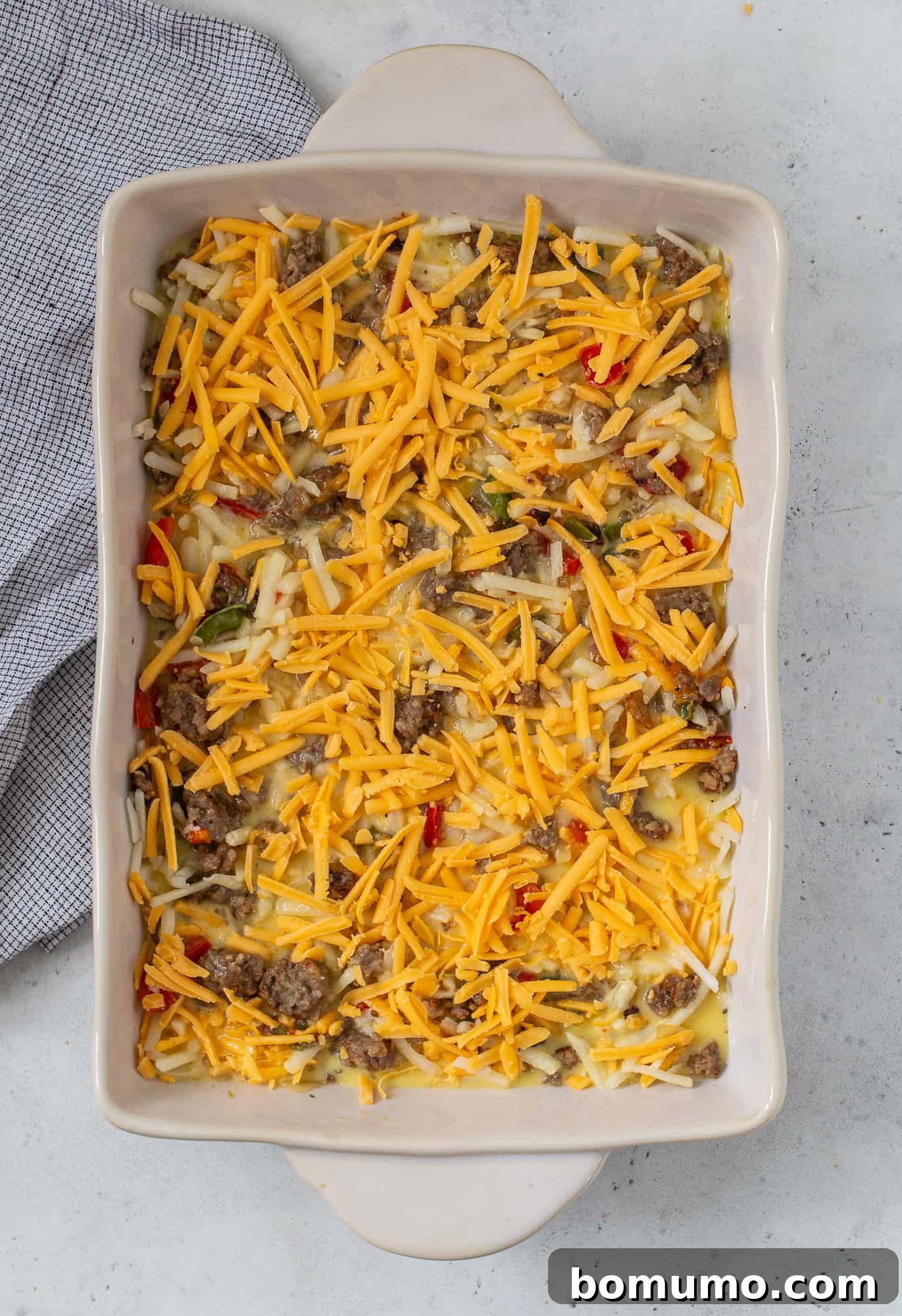 Shredded cheddar cheese added to the top of the unbaked casserole.
