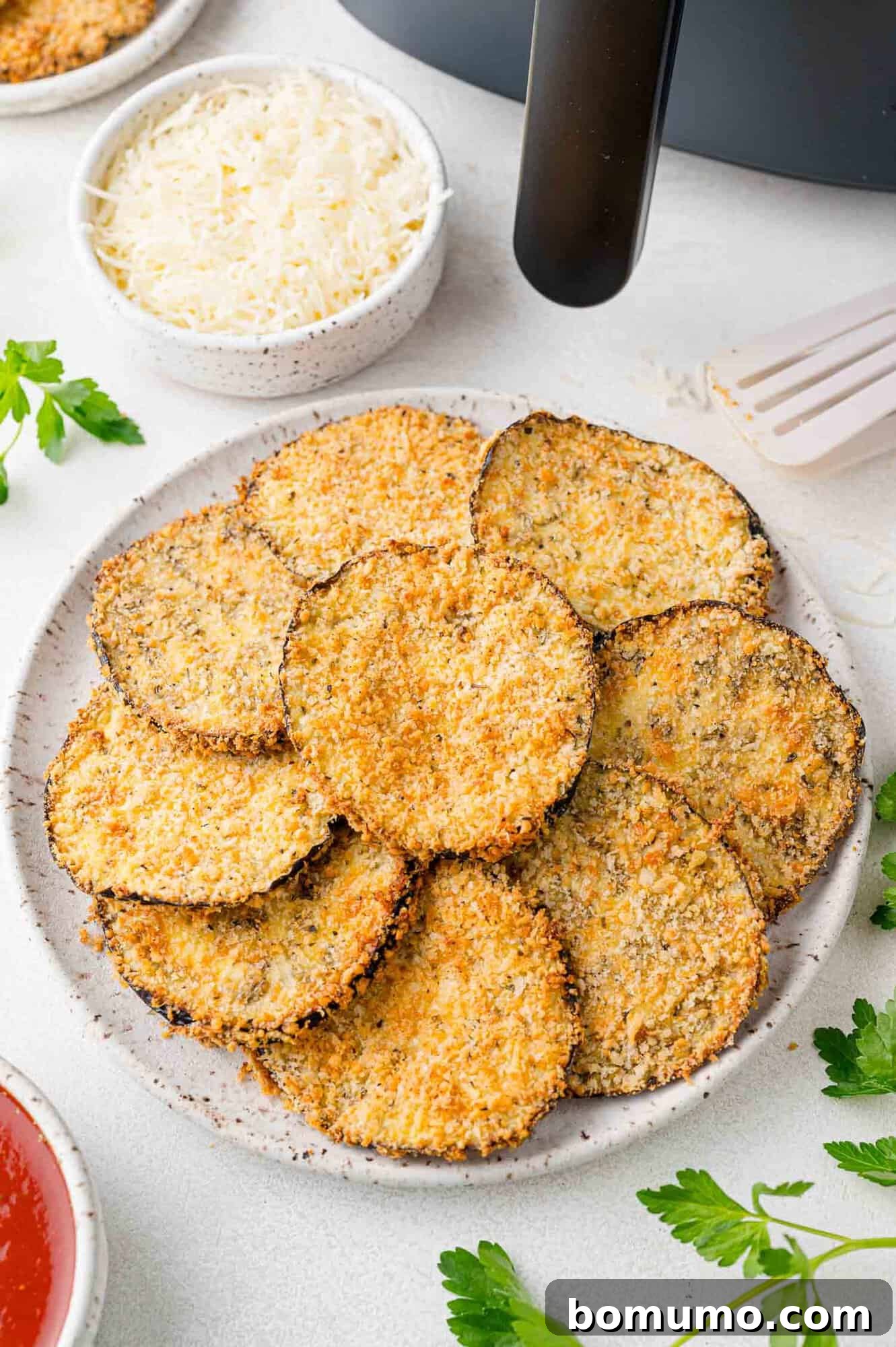 Crispy Air Fried Eggplant 12 Crispy eggplant slices arranged on a plate, air fryer also present in corner of photo.