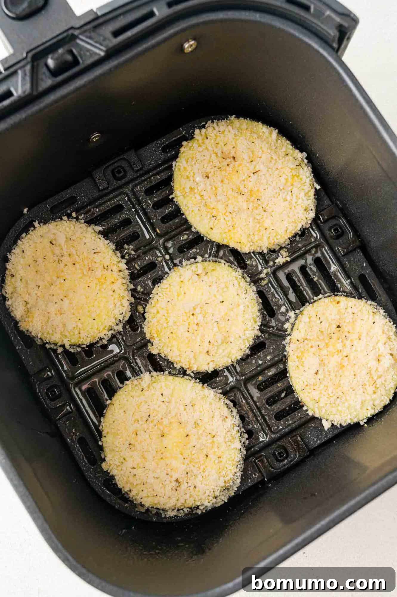 Crispy Air Fried Eggplant 10 Breaded, uncooked eggplant rounds in air fryer basket.