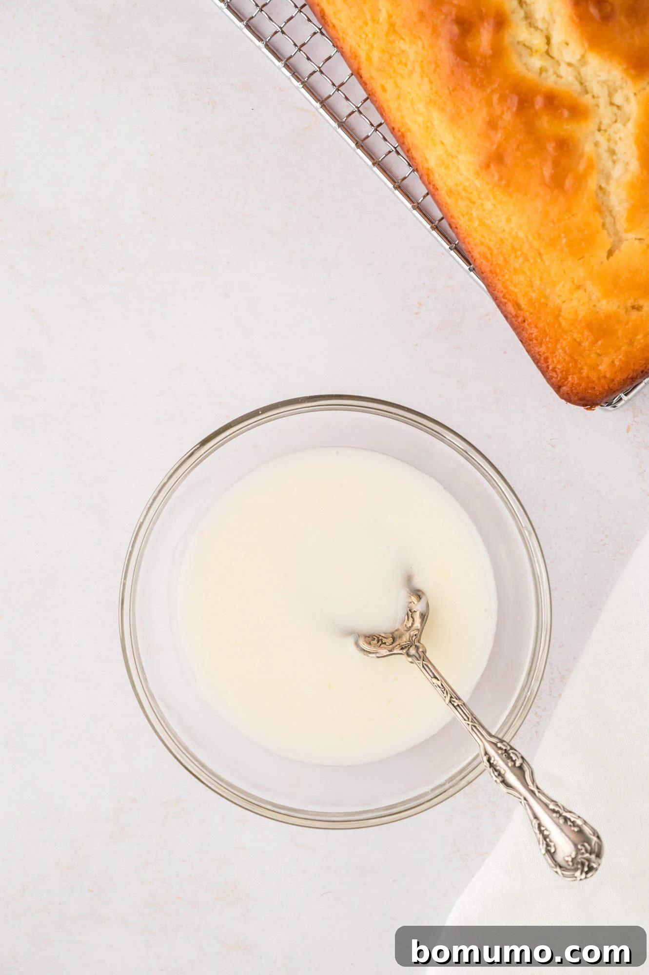 Lemon glaze in a small bowl next to a loaf of bread.