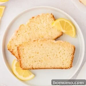 Two slices of lemon bread on a plate with lemon wedges.