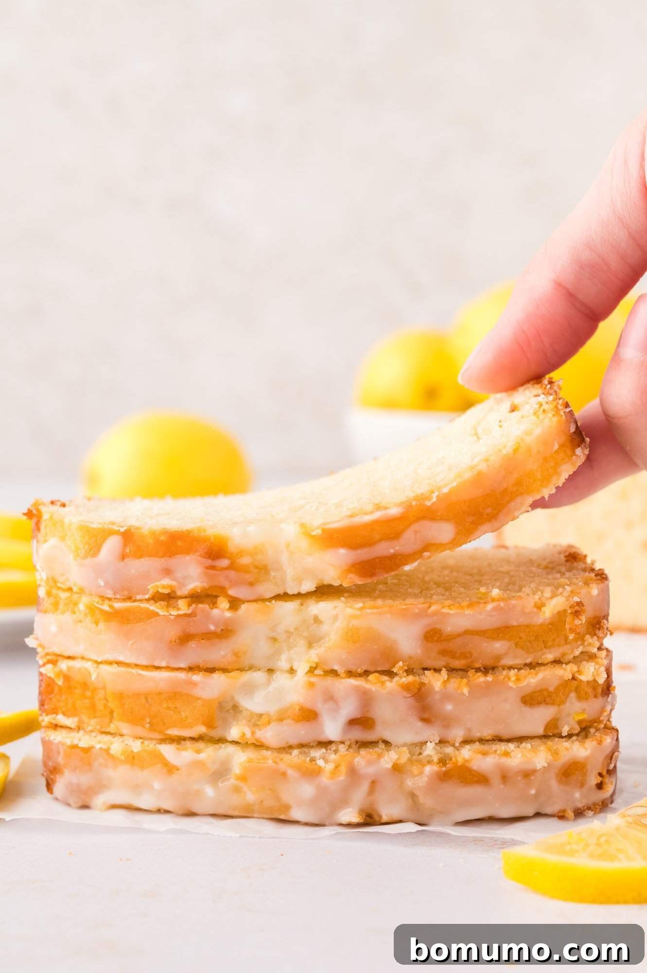 Stack of lemon bread slices, the top slice being lifted by a hand.