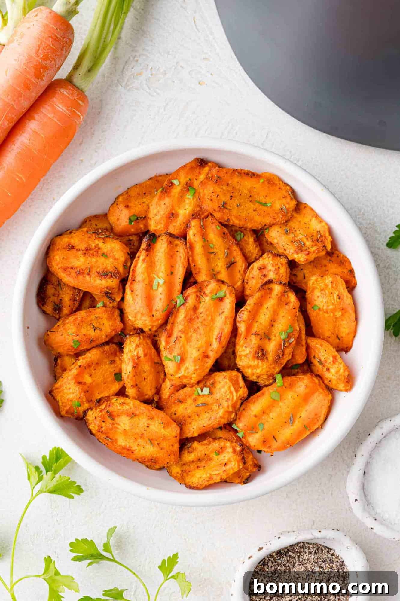 Crinkle cut air fryer carrots served in a white bowl, with fresh carrots nearby.