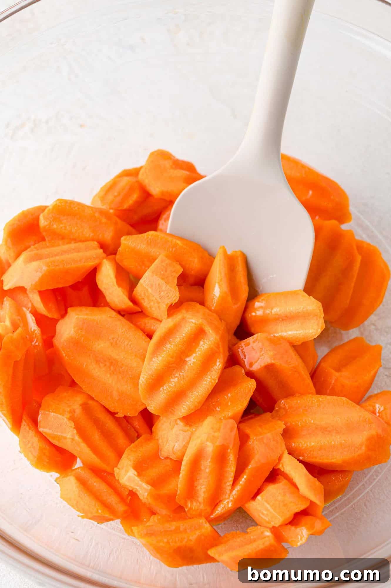 Hand mixing carrot slices with olive oil and spices in a large bowl.
