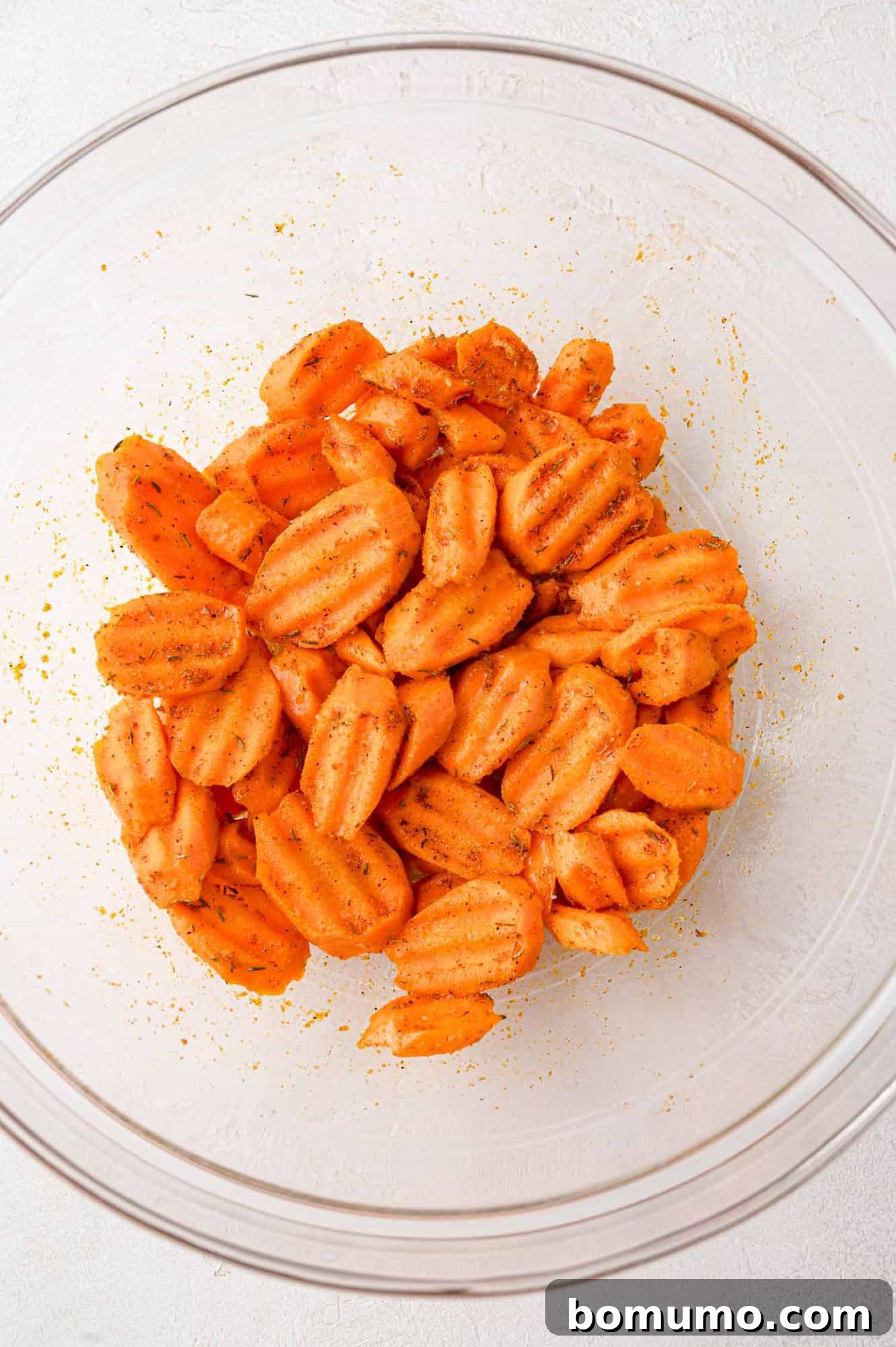 Seasoned raw carrots glistening in a clear bowl, perfectly coated and ready for the air fryer.