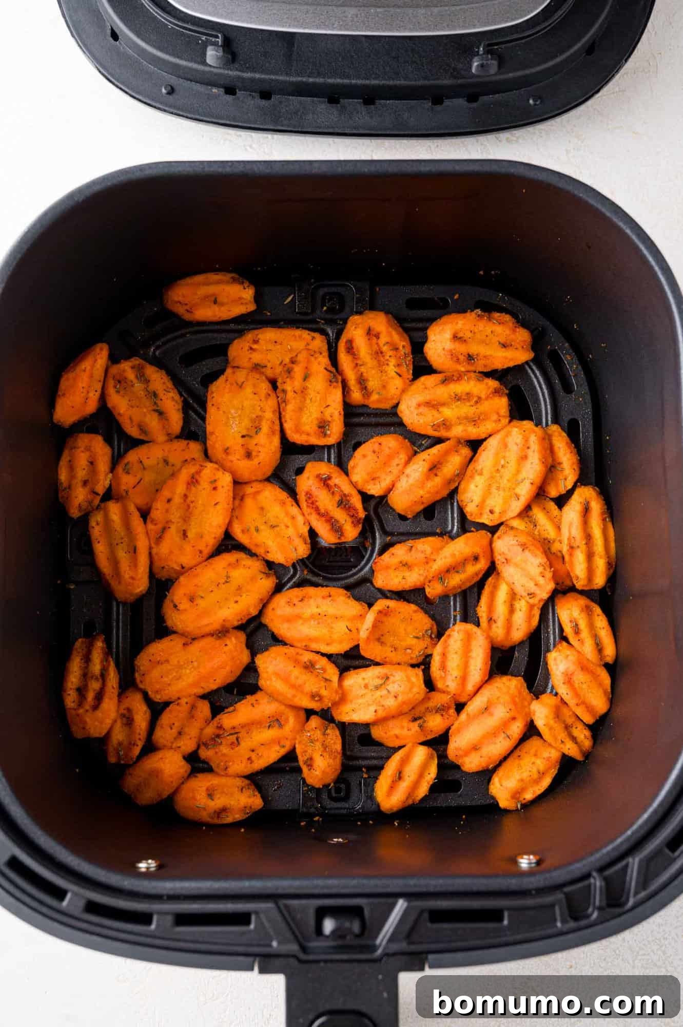 Neatly arranged sliced carrots in the air fryer basket, before cooking.