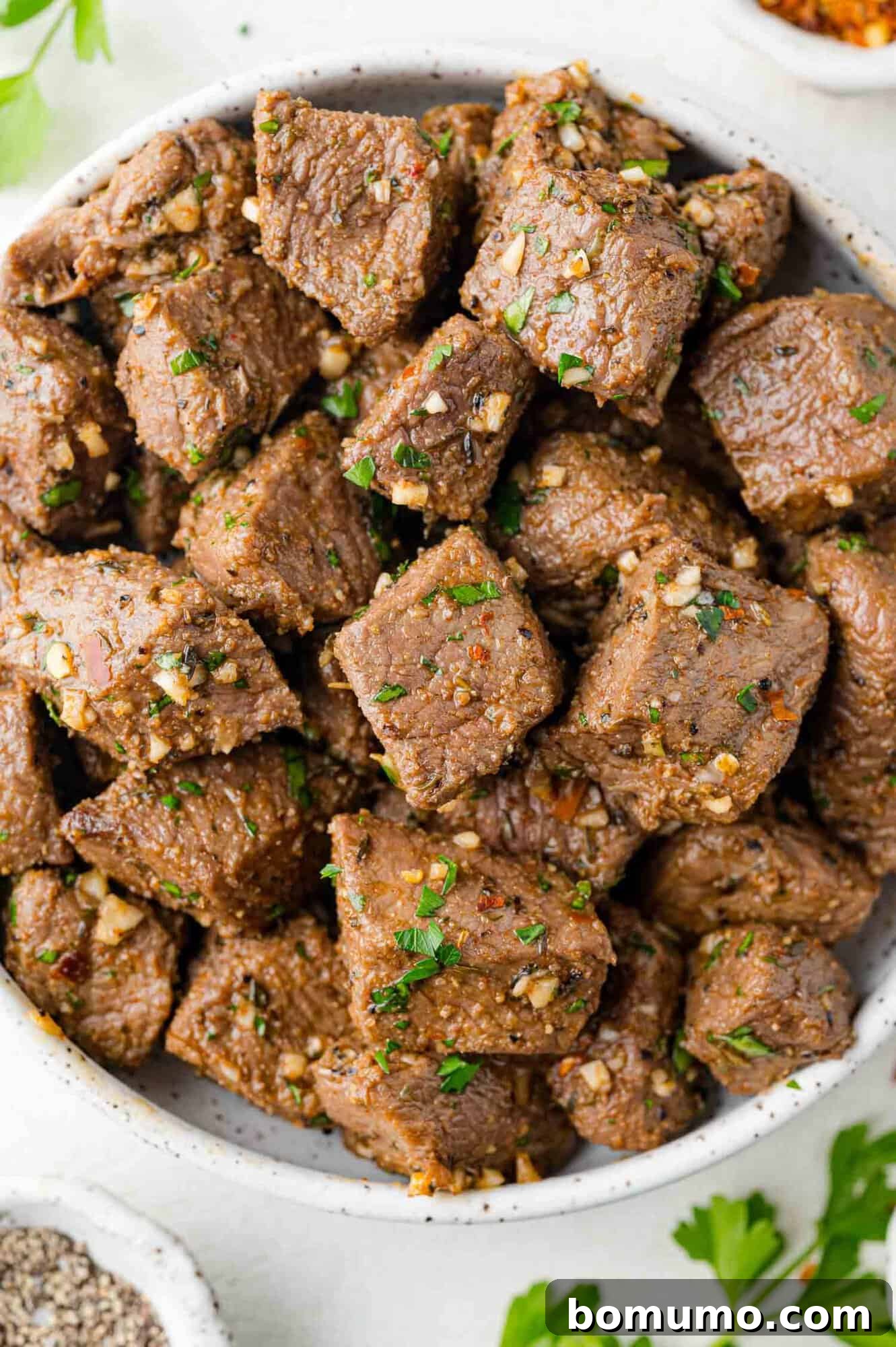 A bowl brimming with perfectly cooked air fryer steak bites, garnished with fresh garlic and vibrant parsley, ready to serve.