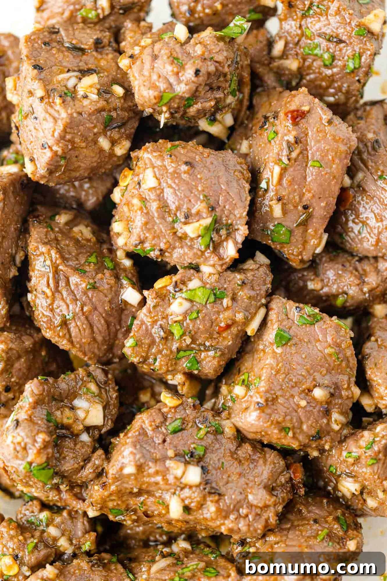 Cooked steak bites, beautifully coated and glistening with the rich garlic butter, showing even distribution of herbs.