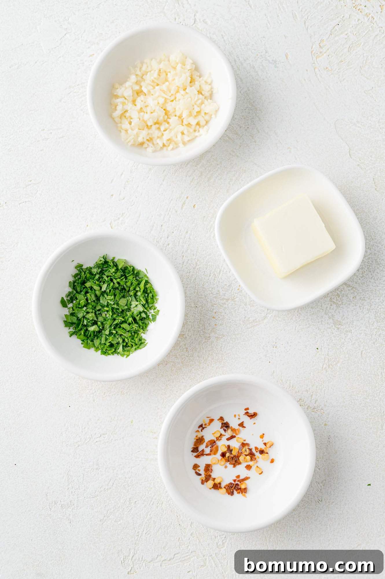 The essential ingredients for the optional garlic butter, featuring a stick of butter, freshly minced garlic cloves, and bright green parsley sprigs.