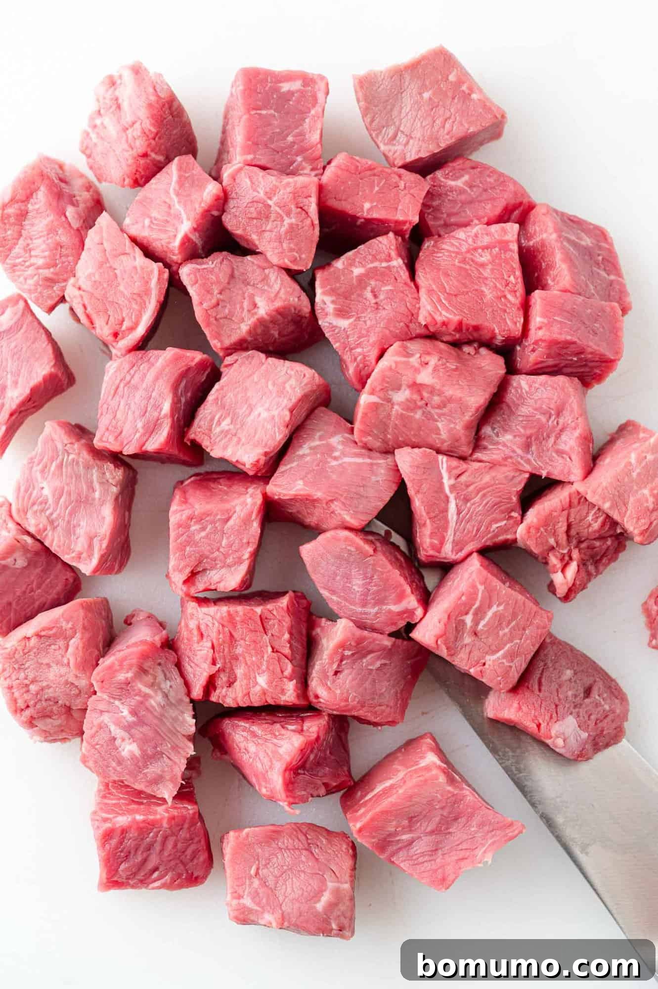 Raw sirloin steak cut into perfectly uniform bite-size pieces on a wooden cutting board, ready for the marinade.