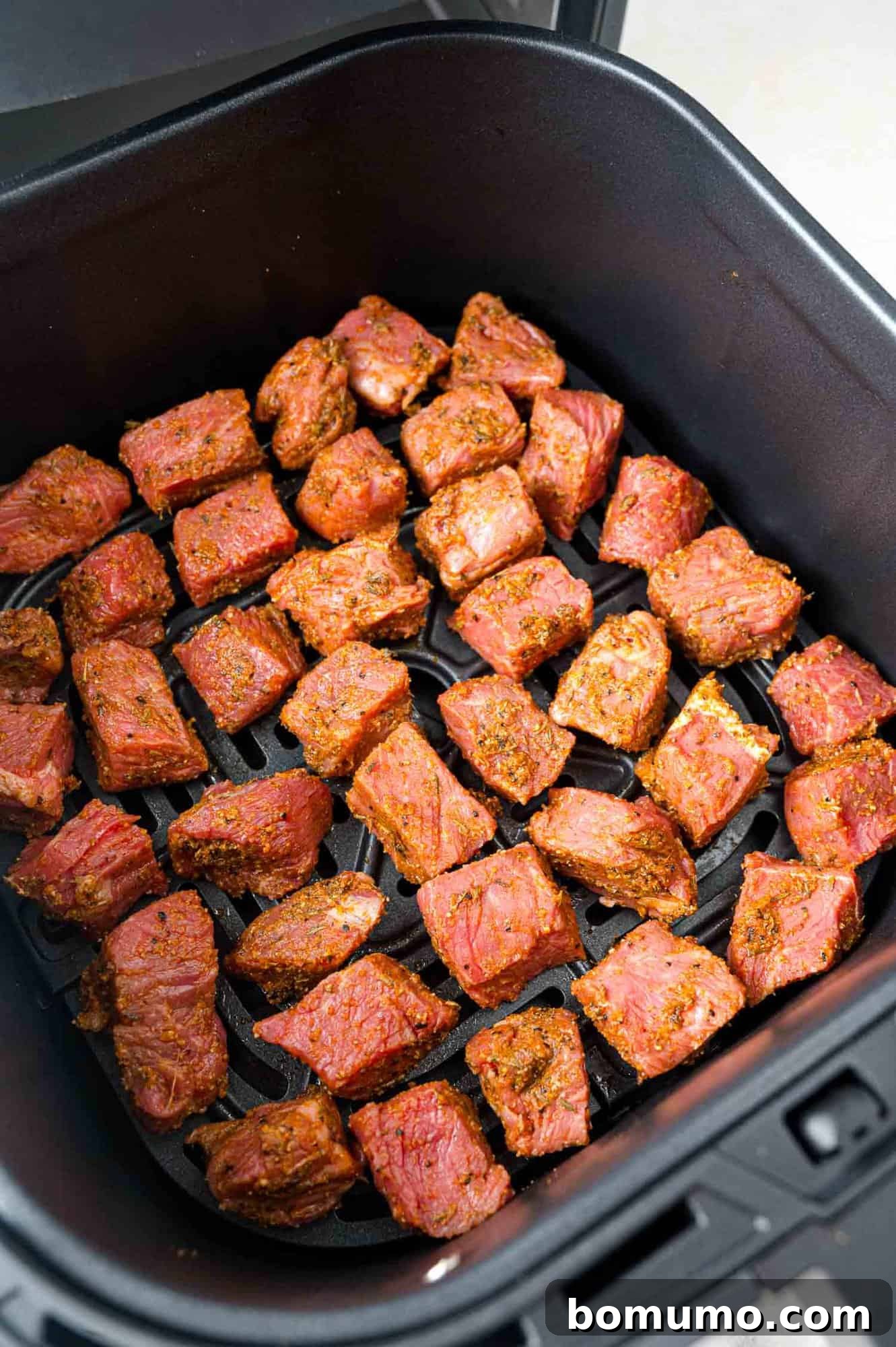 Marinated steak bites precisely arranged in a single layer within the air fryer basket, awaiting cooking.