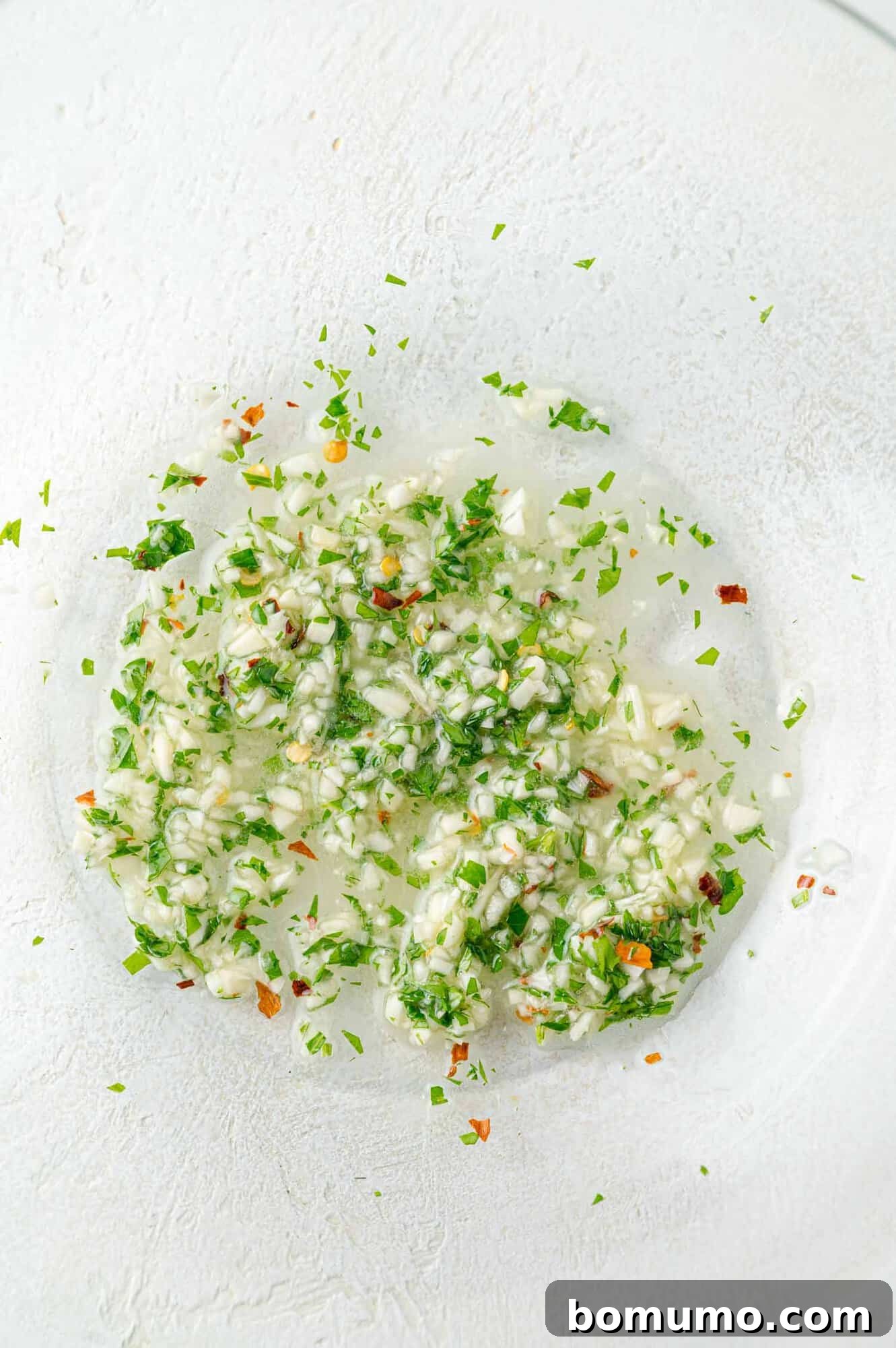 A bowl of freshly prepared garlic butter mixture, vibrant with minced garlic and green parsley, anticipating the cooked steak.