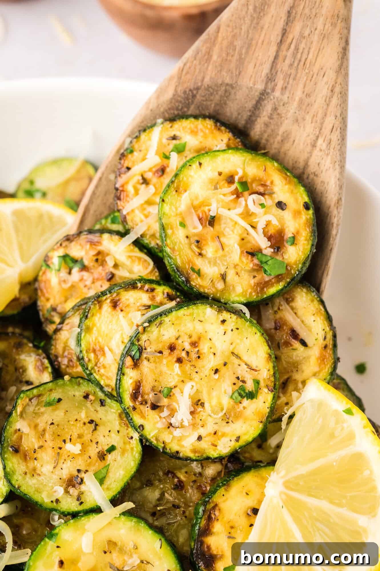 Sautéed zucchini on a wooden spoon, topped with parmesan cheese, highlighting its tender, garlicky texture.