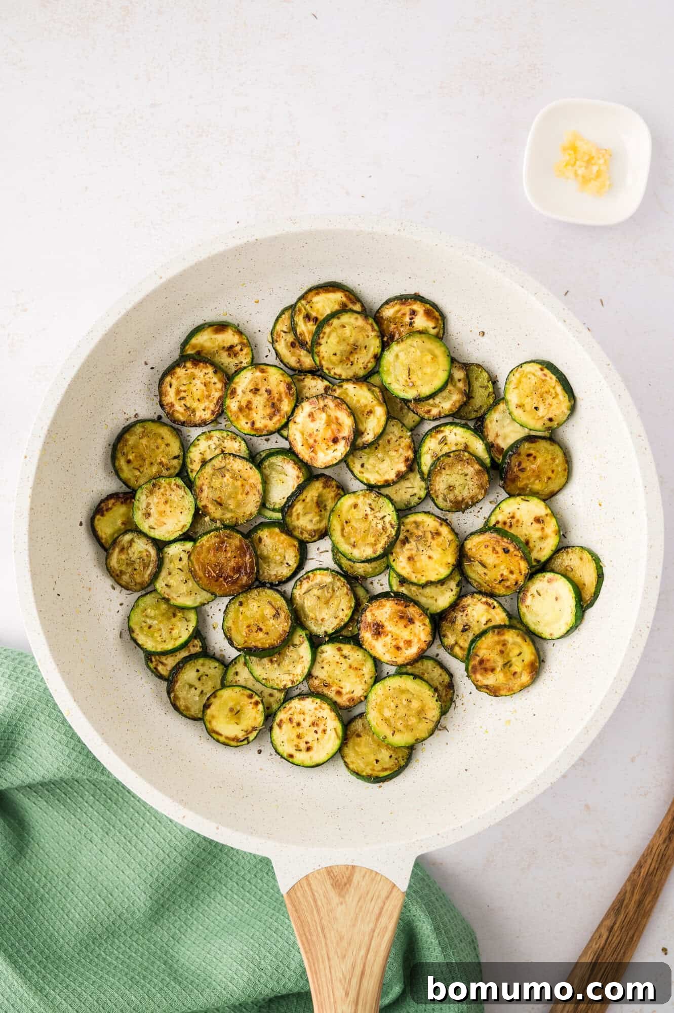Perfectly browned zucchini slices in a white frying pan, indicating readiness.