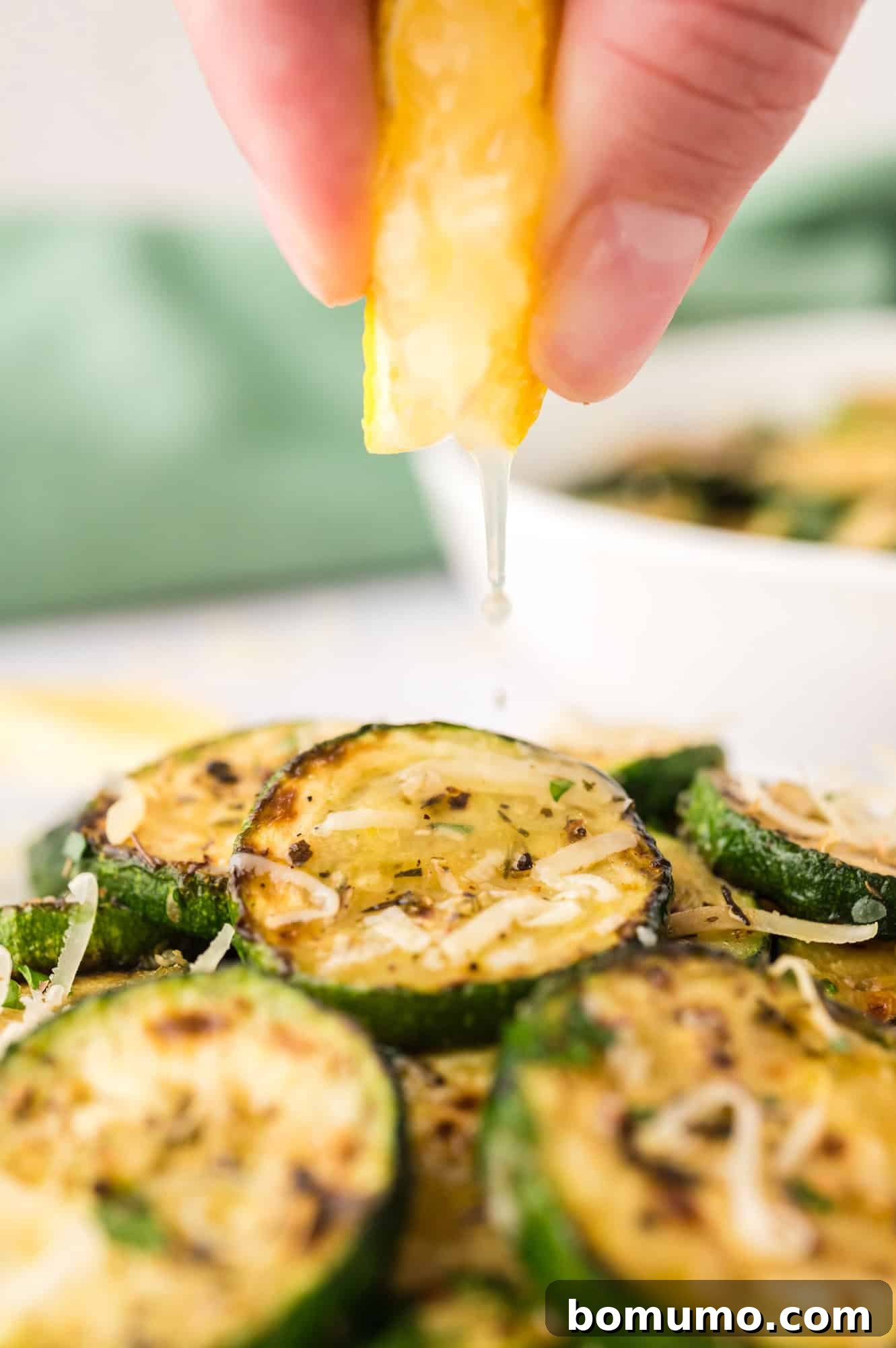 A fresh lemon wedge being squeezed over a serving of vibrant sautéed zucchini slices.