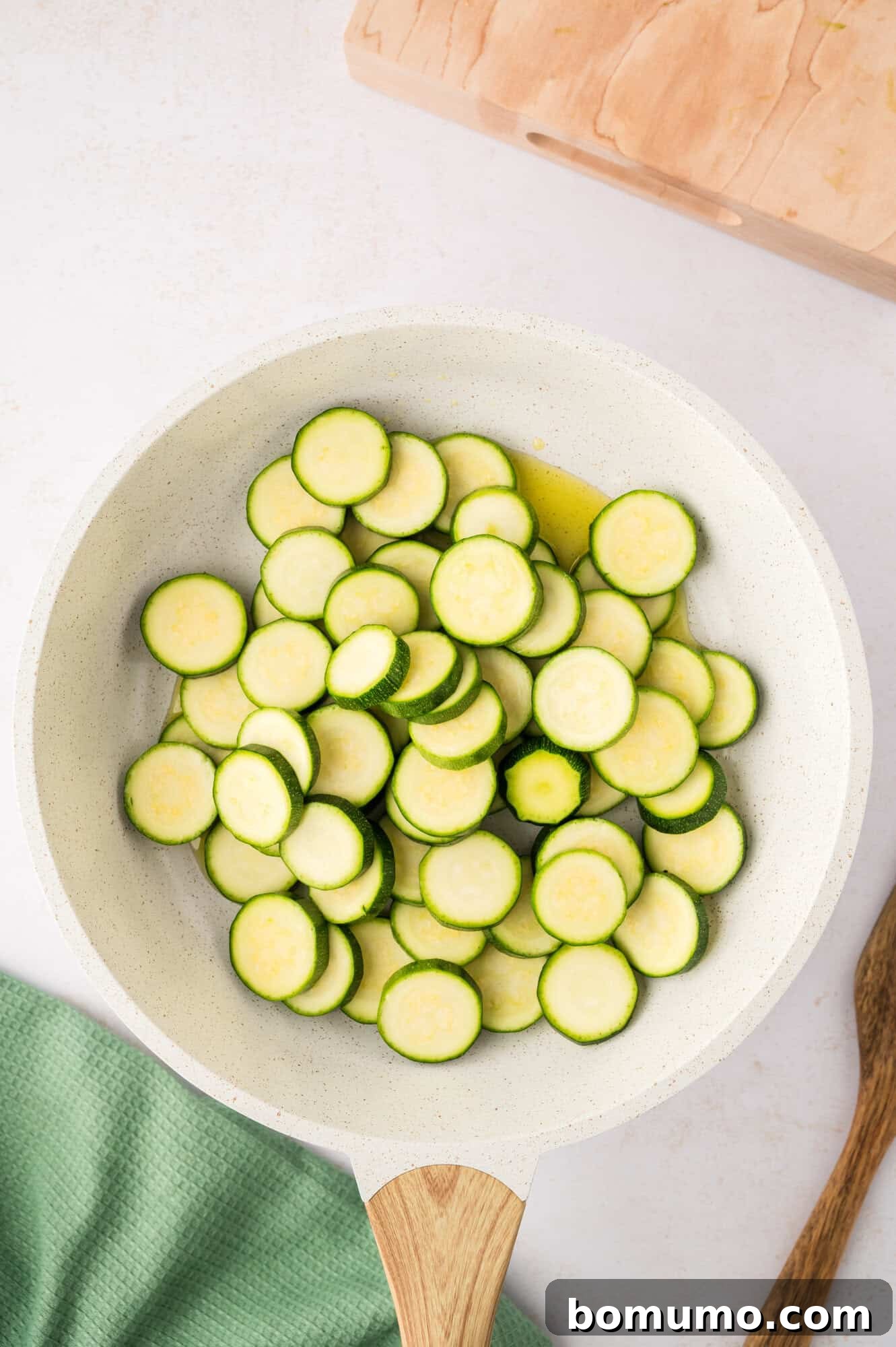 Zucchini slices freshly added and piled in a hot frying pan, about to be spread out.