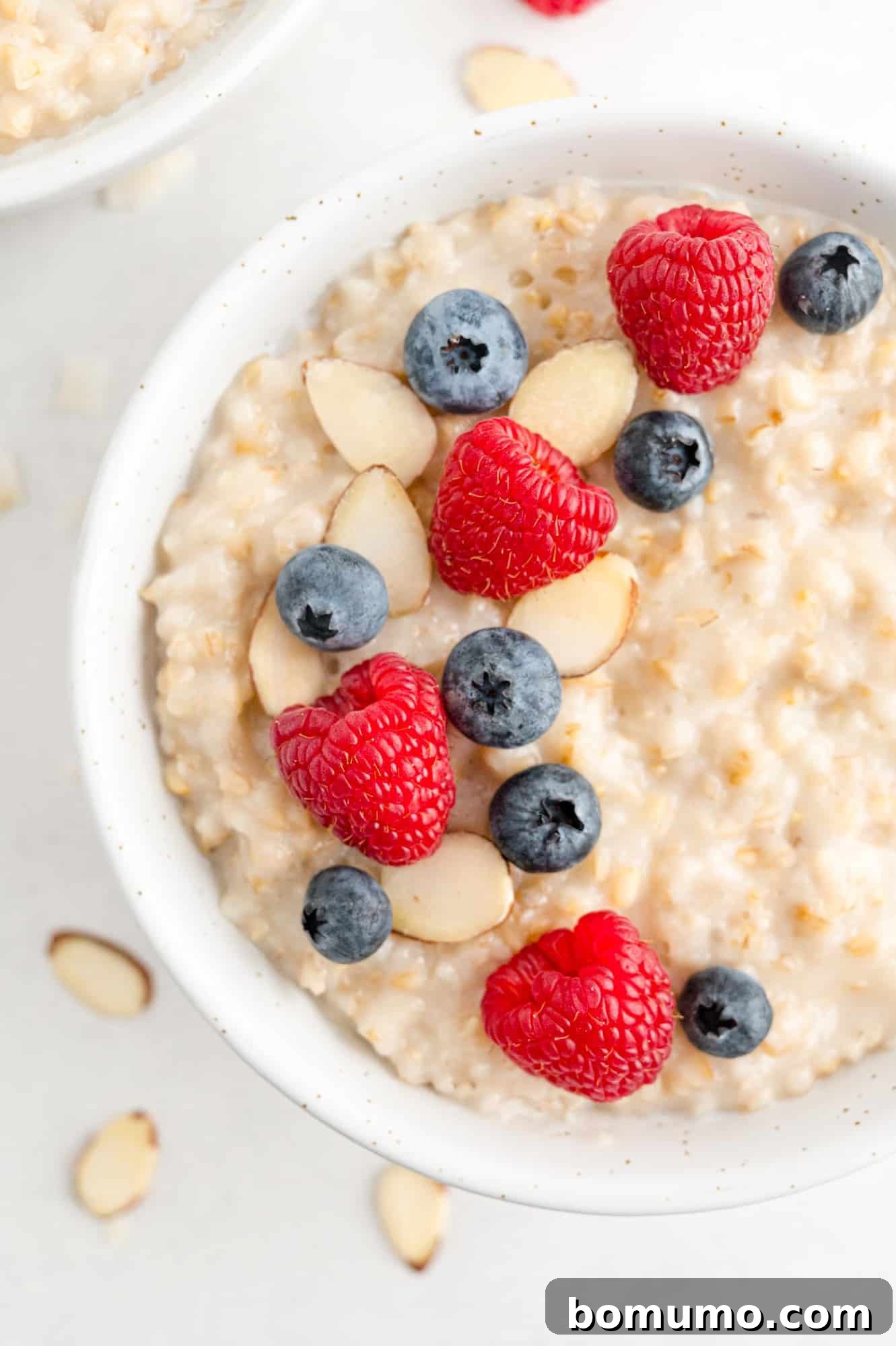 Delicious crockpot oatmeal in a white bowl, generously topped with fresh raspberries, blueberries, and crunchy almonds, ready for a healthy morning.