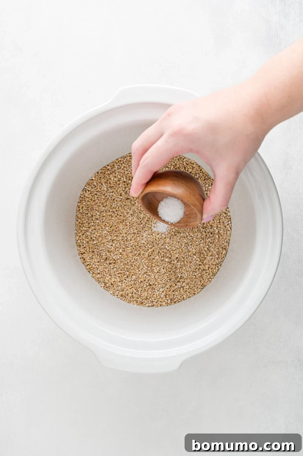 A hand gently sprinkles a pinch of salt into a white bowl, enhancing the flavor of the grains within.